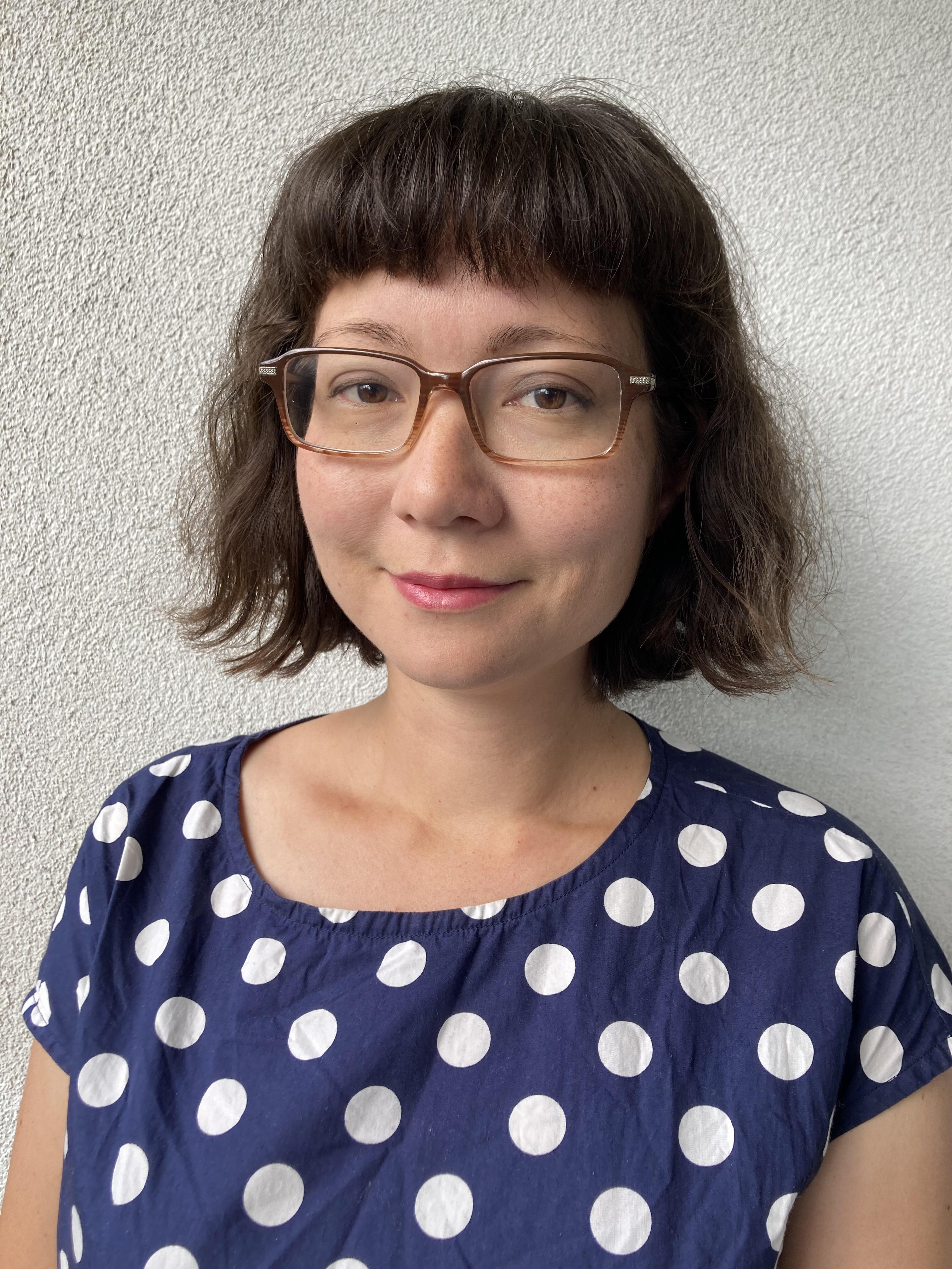 A woman with dark hair in a bob, wearing glasses and a blue and white spotty tshirt