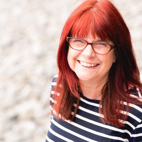 a white woman with long red hair wearing glasses and a stripy top