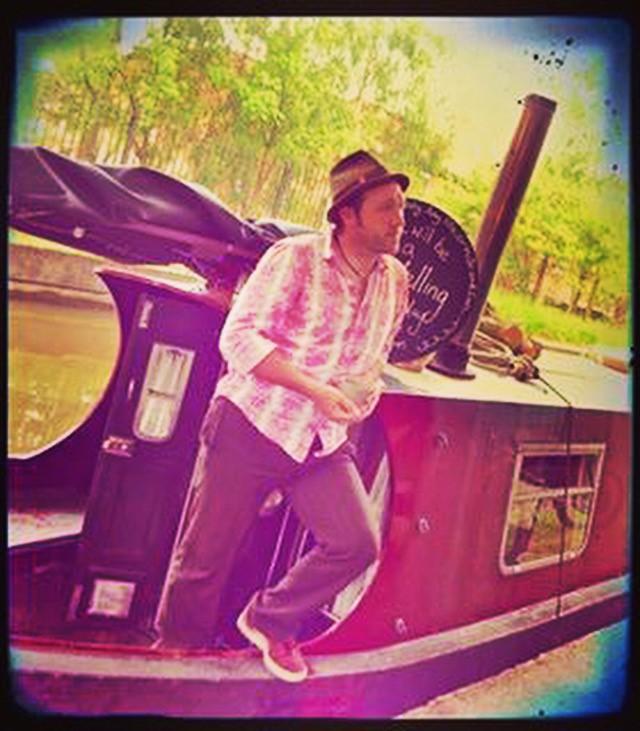 Ian Douglas is stood on a canal boat and wearing a hat.
