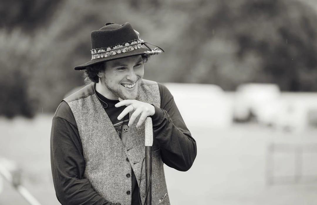 Black and white of Ceri telling stories. He is wearing a hat and holding a walking stick in his hands.