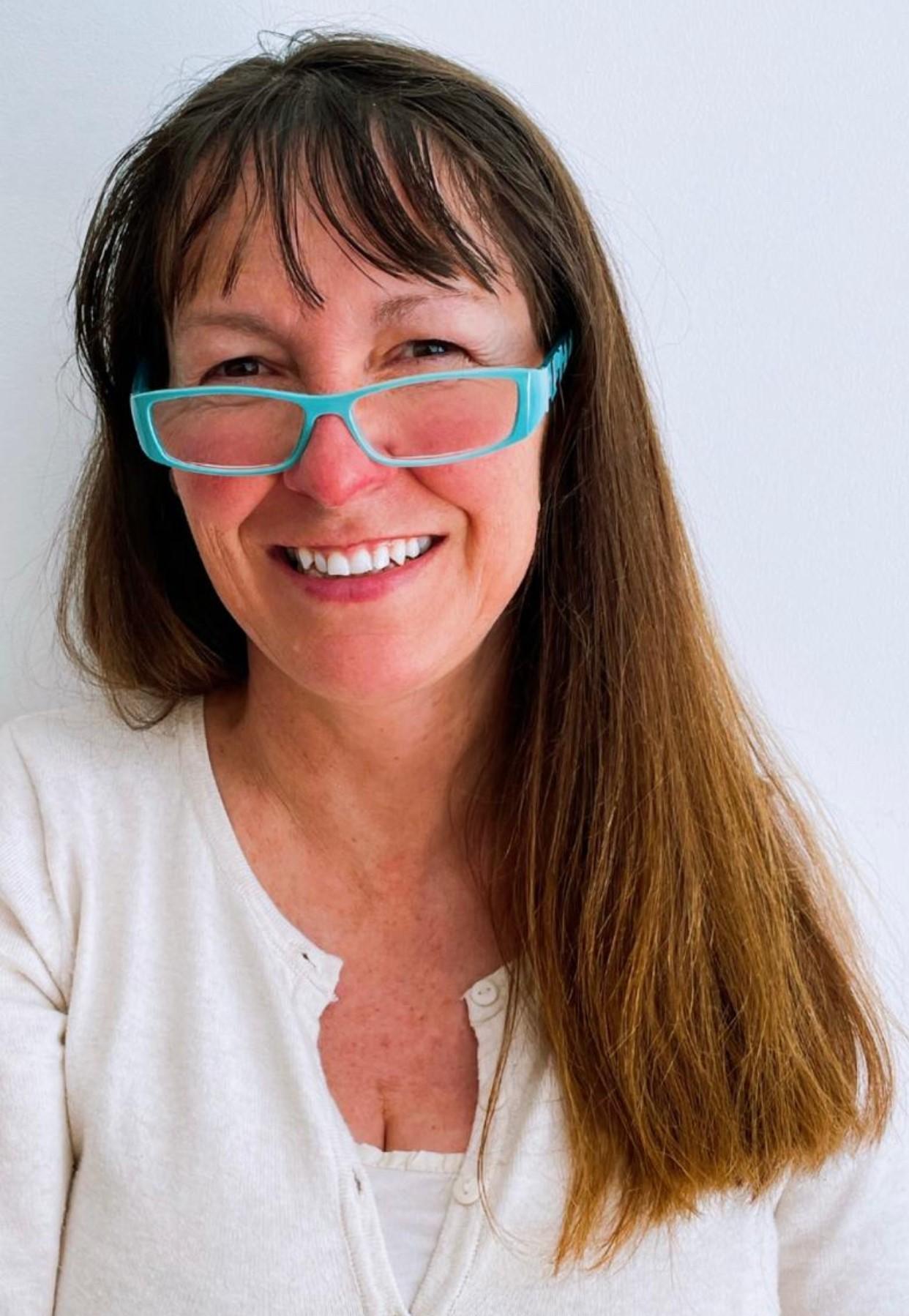 Hedydd has long straight brown hair and wears blue rimmed glasses.