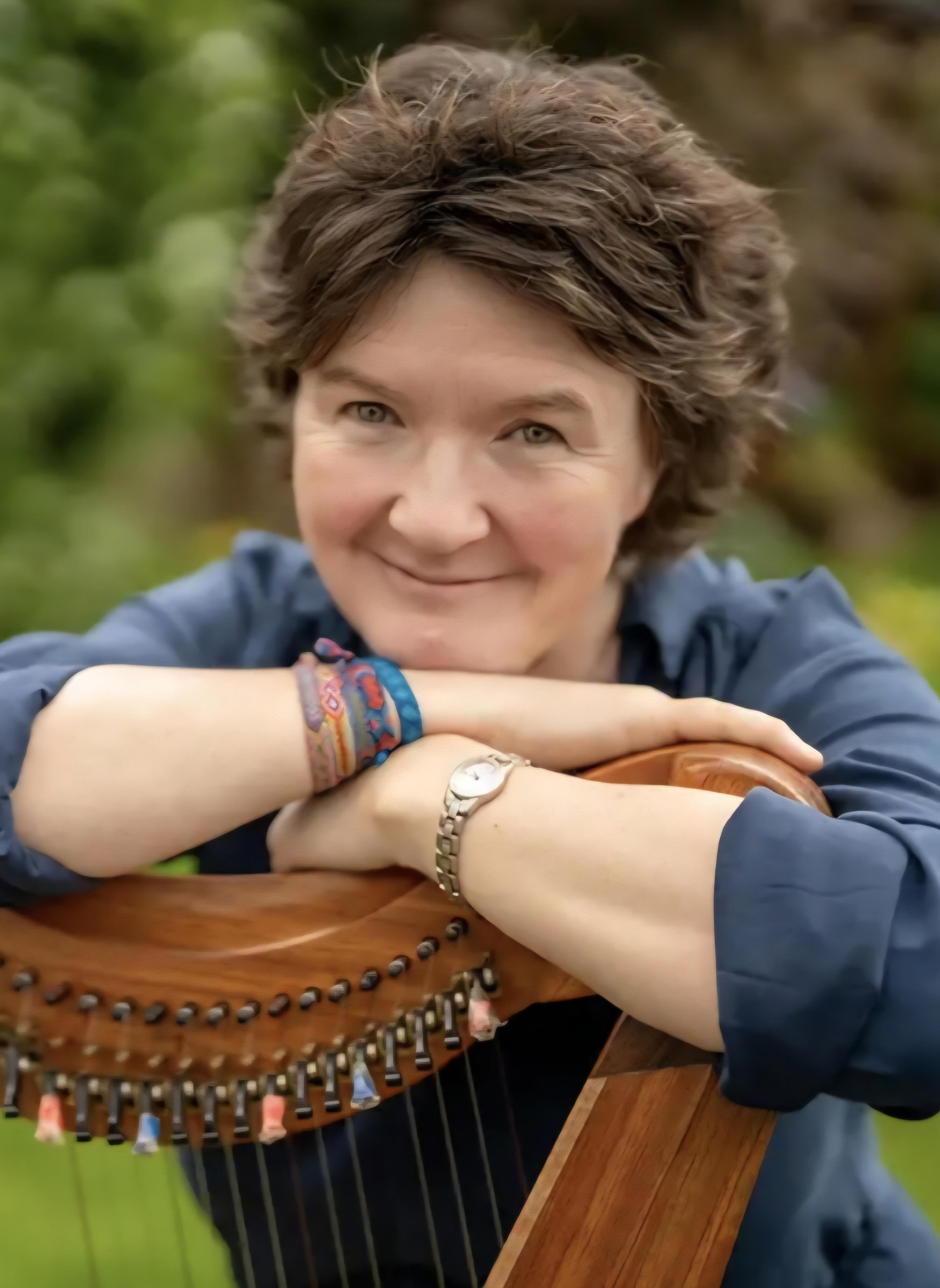 Stacey is leaning on a wooden harp and has short brown hair.