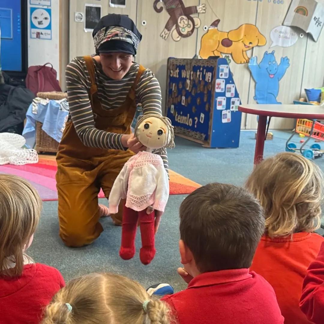 Naomi Doyle holding up a puppet in front of children in a school.