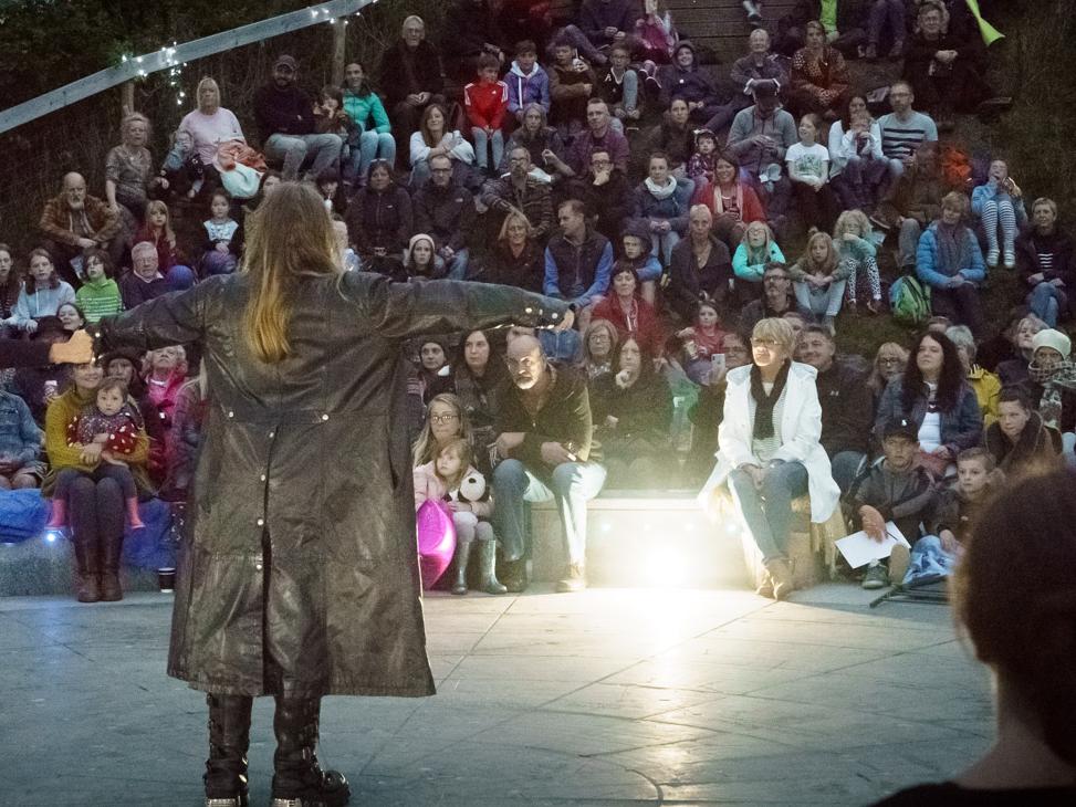 A photograph of storytellers speaking out to an ampitheatre audience on stage.