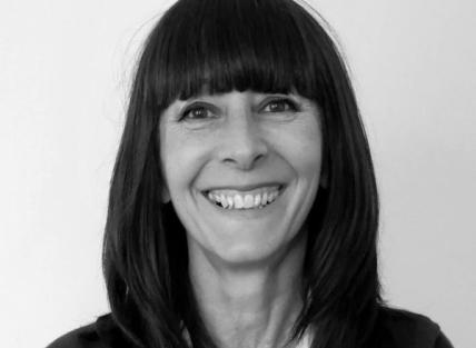 a black and white head and shoulders photo of Jane Wells, a white woman with long dark hair wearing a dark coloured jacket