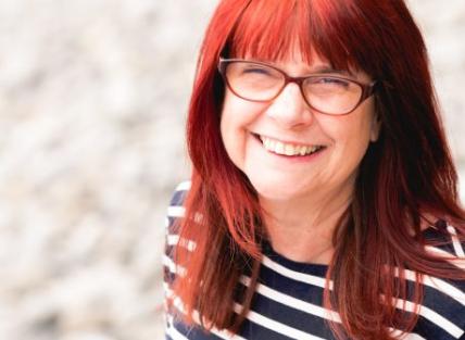 a white woman with long red hair wearing glasses and a stripy top