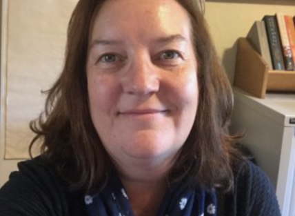 a white woman with shoulder length brown hair, wearing a blue and white scarf