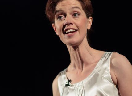 a young white woman with brown hair tied up, wearing a white, silky top