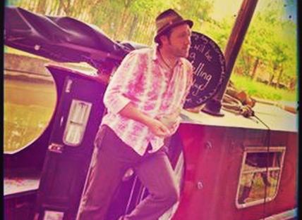 Ian Douglas is stood on a canal boat and wearing a hat.