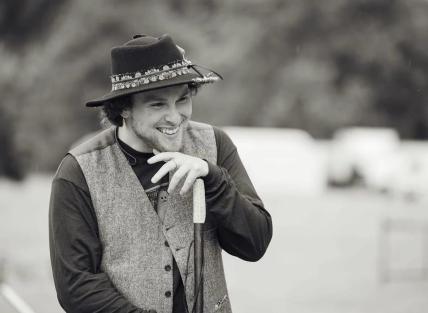 Black and white of Ceri telling stories. He is wearing a hat and holding a walking stick in his hands.