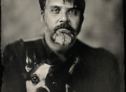 A black and white photo of Dan with a beard and a dog sat on his lap