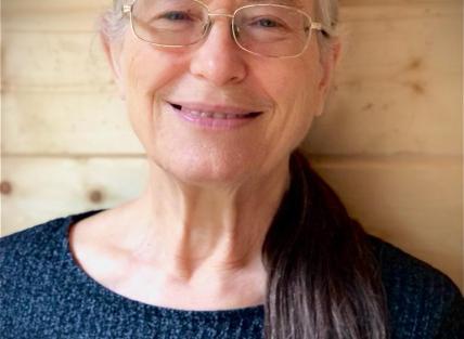 Fiona has long blondish hair and is wearing glasses and a blue sweater.