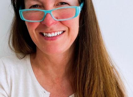Hedydd has long straight brown hair and wears blue rimmed glasses.